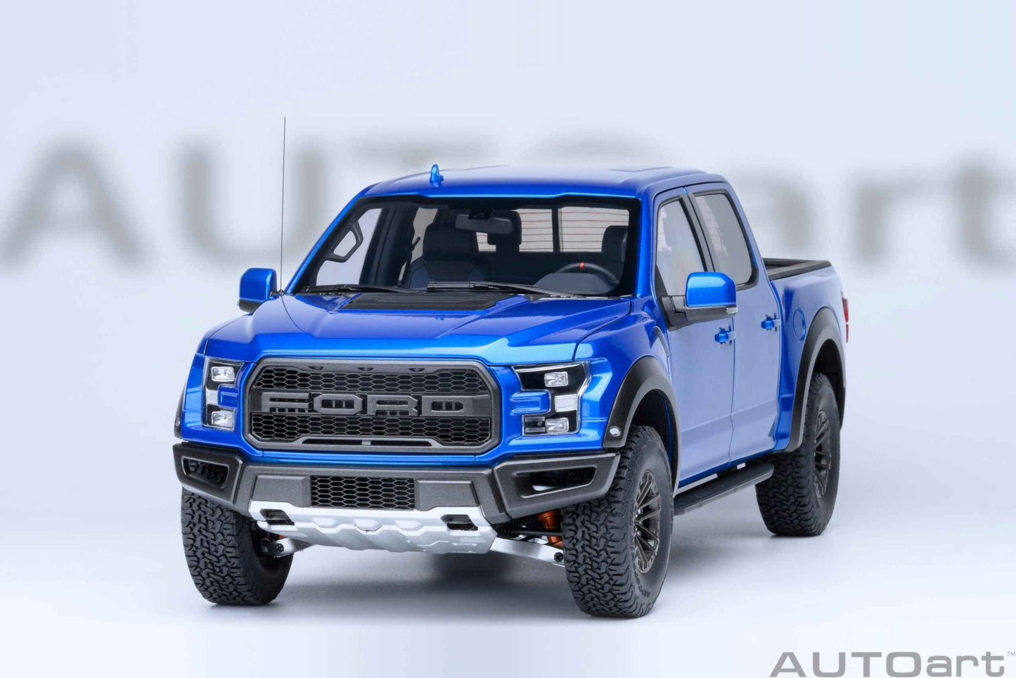 Blue pickup truck model facing forward with black grille, headlights, and textured tires