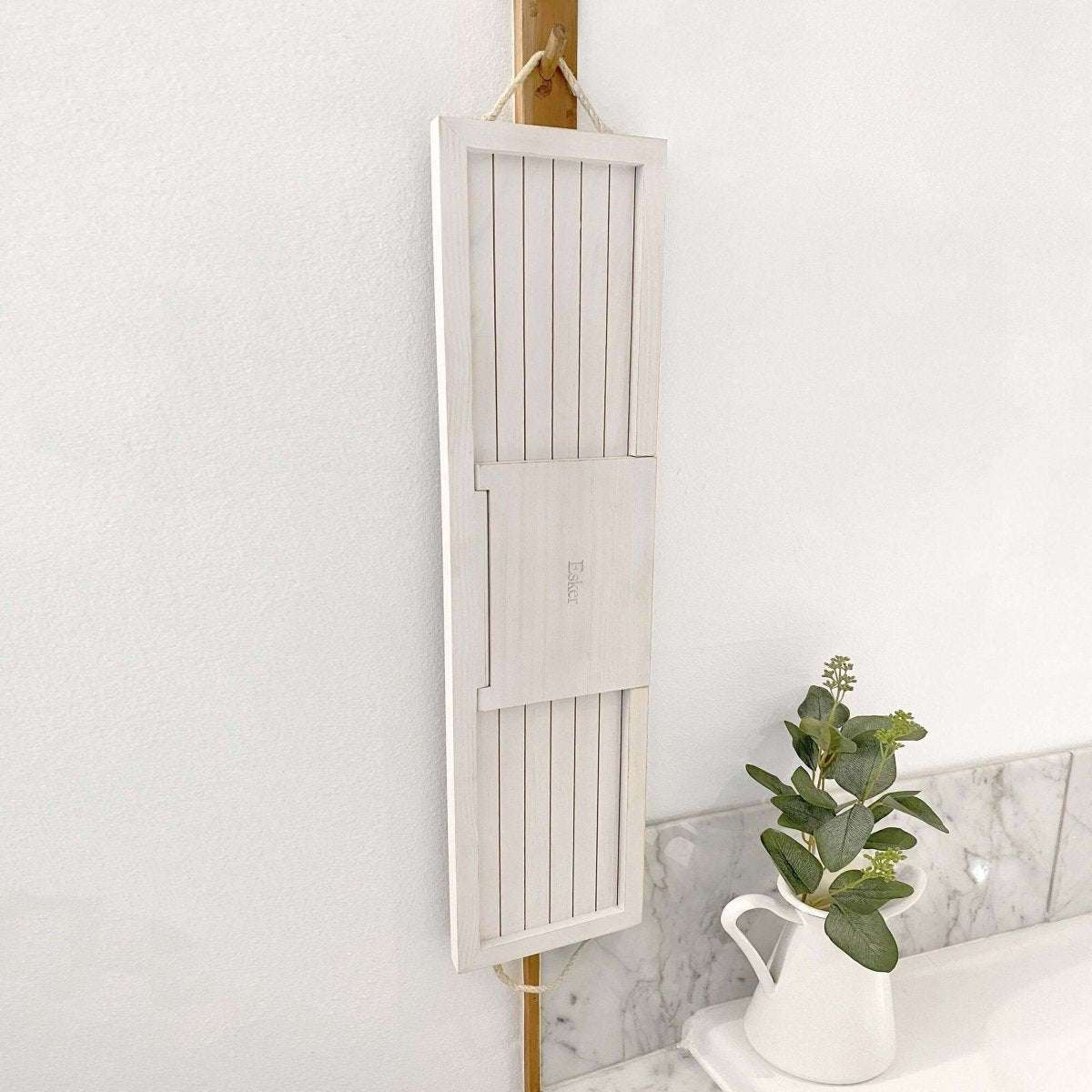 Bath board with white slatted panels and hanging loop, folded open against a wall.