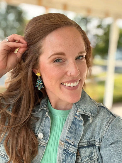 Woman wearing acrylic Christmas tree earrings with confetti design and gold star accents