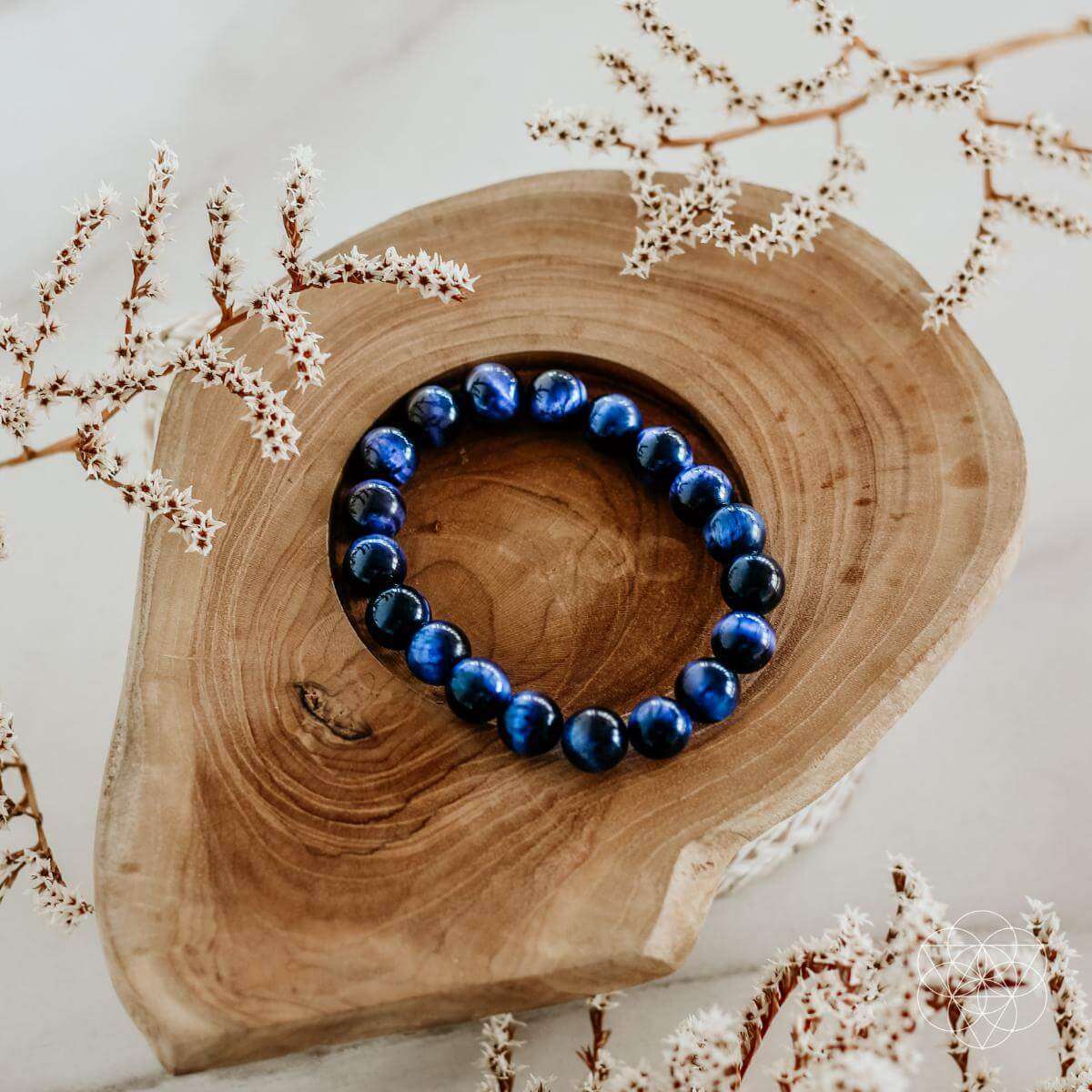 Blue beaded bracelet with dark round stones, shown on a wooden slice