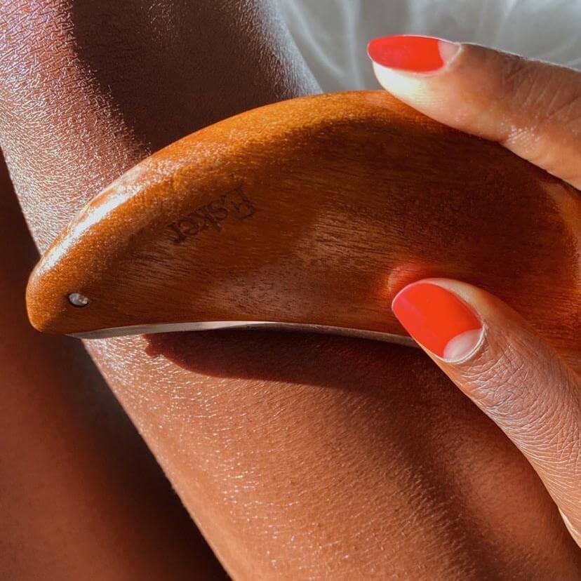 Curved wooden exfoliator tool on bare skin