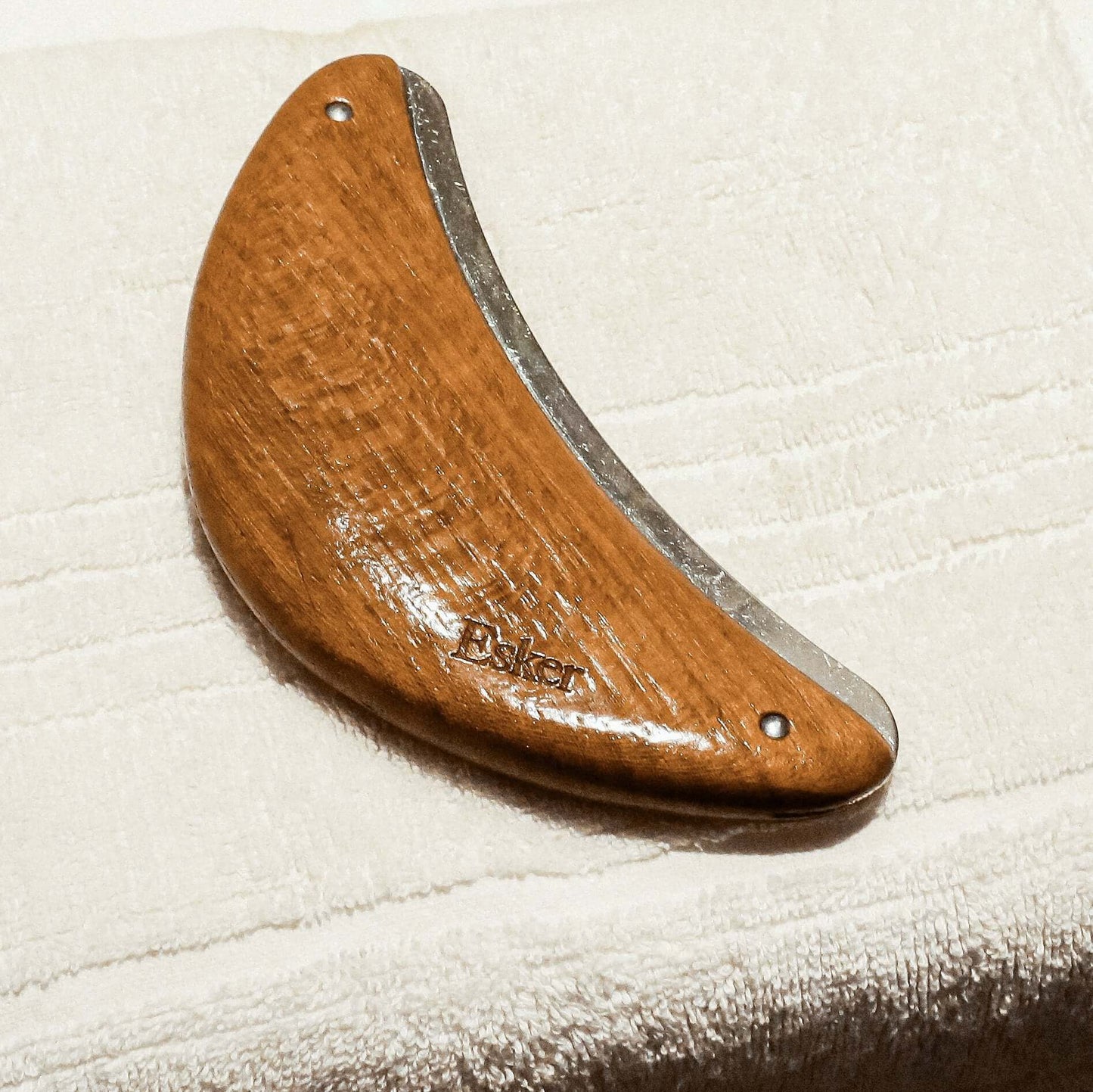 Curved wooden body exfoliator tool with silver edge and rivet details on a towel