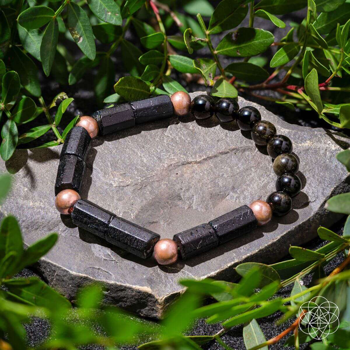 Copper-tone and black bead bracelet with rectangular dark spacer bars on rock