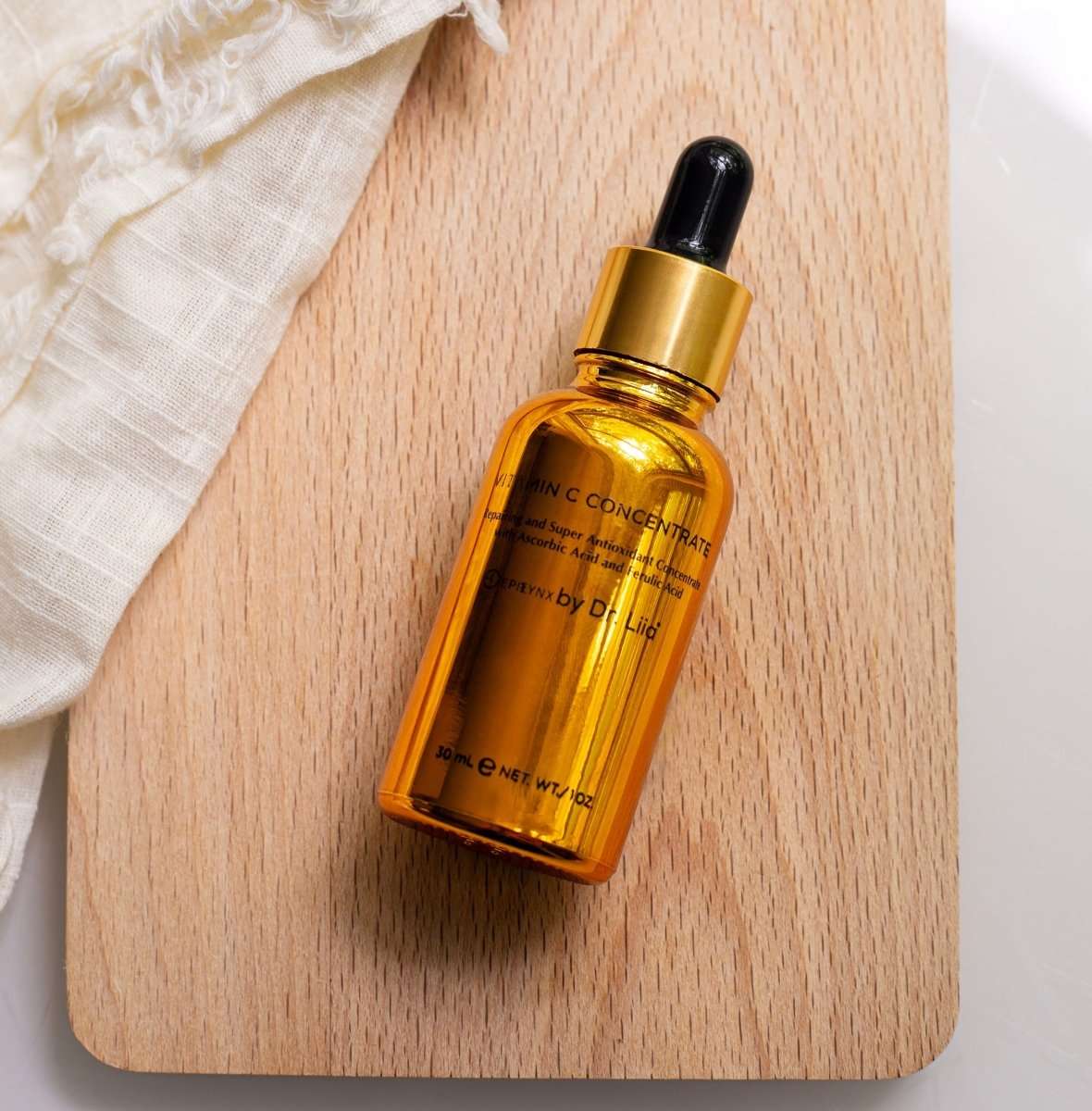 Gold amber serum bottle with black dropper, on wooden board
