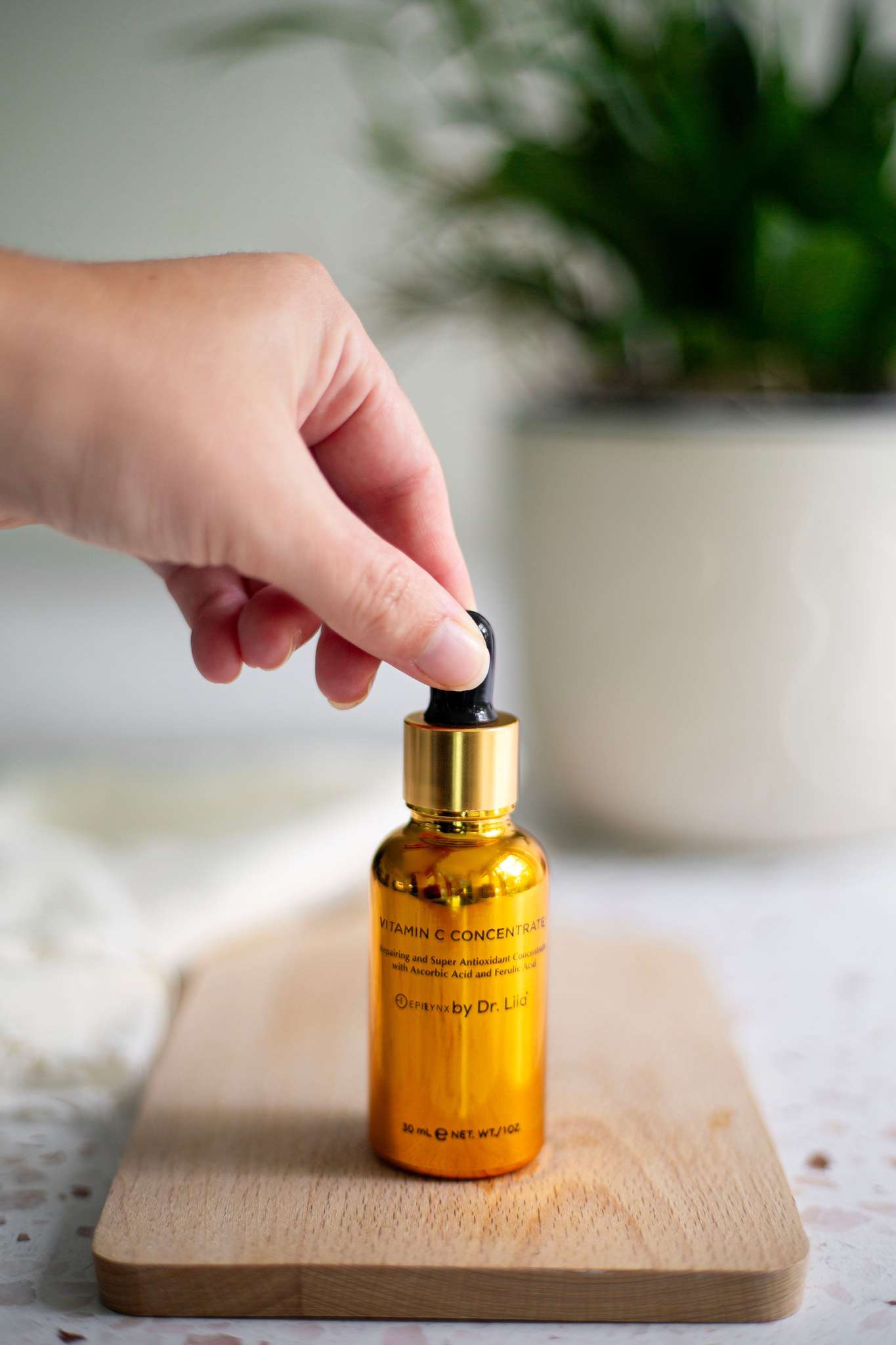 Hand holding black dropper above amber Vitamin C serum bottle
