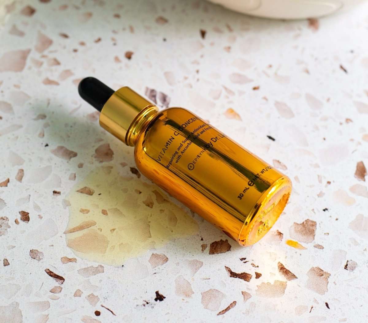 Amber vitamin C serum bottle with black dropper on speckled surface