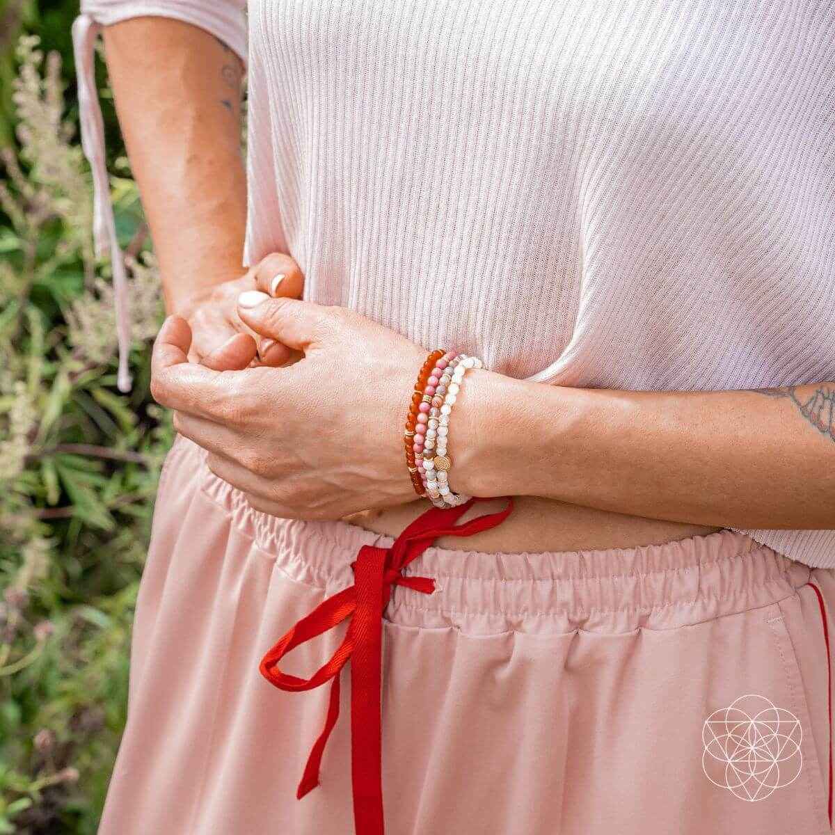 Pink and red bead bracelets with gold-tone center charm on a wrist