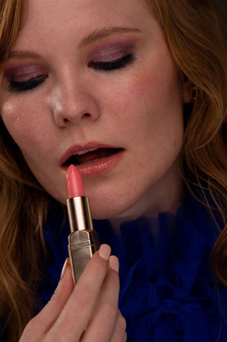 Pink lip gloss applied on lips with a gold-capped tube held near mouth