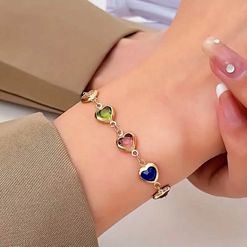 Heart charm bracelet with multicolor stones worn on wrist; gold-tone chain and hearts