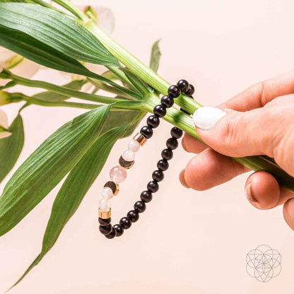 Shungite bracelet held near green leaves, black beads with pink stones and gold caps
