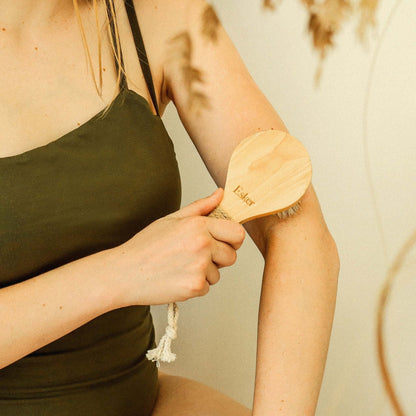 Wooden dry brush with rounded natural bristle head being rubbed on an arm