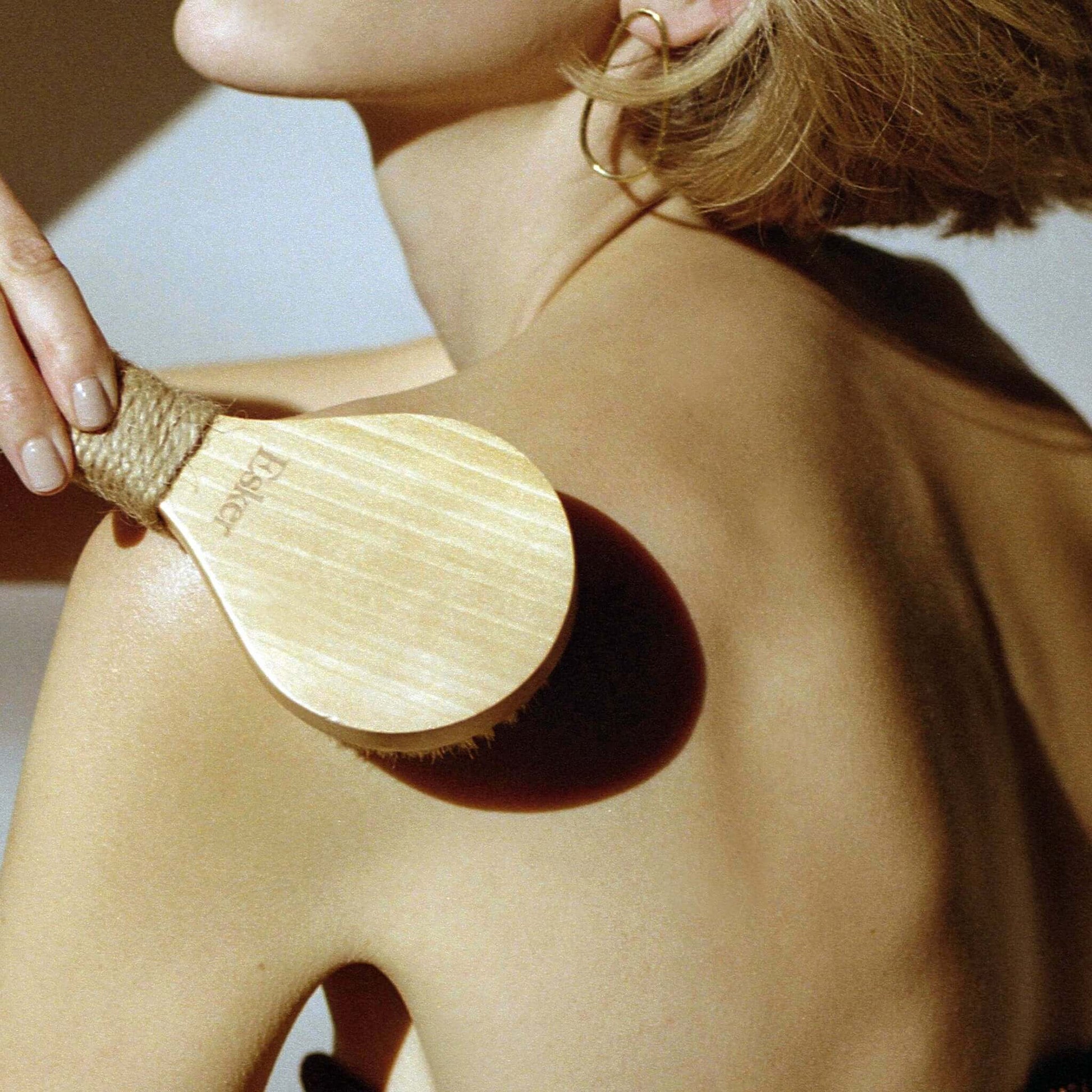 Wood-handled dry body brush with natural bristles in use on skin