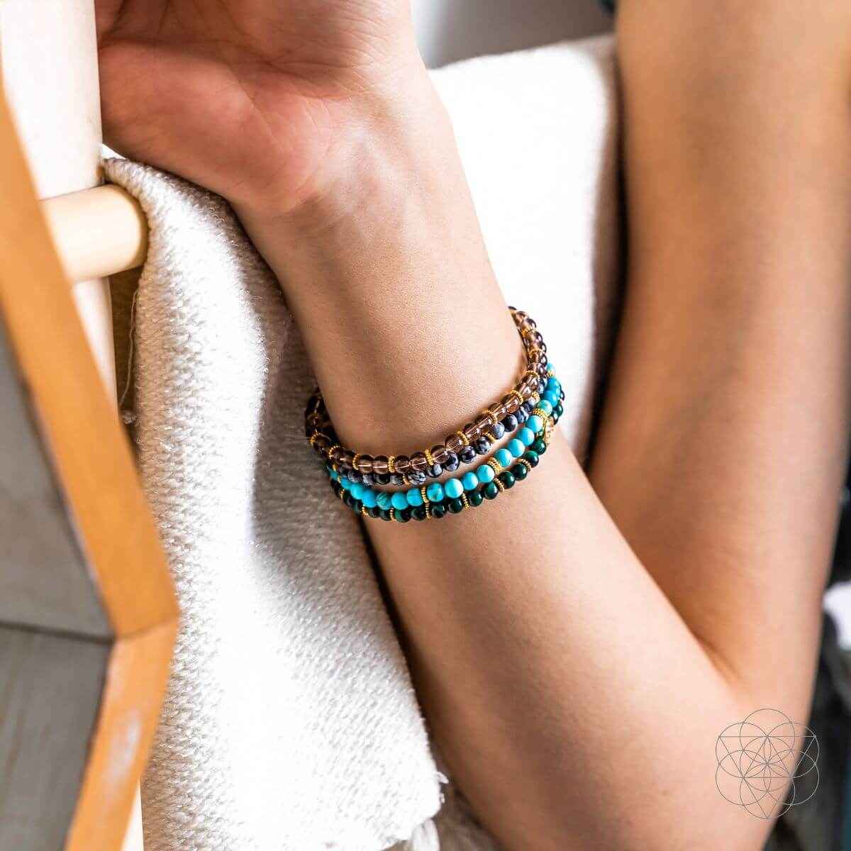 Four stacked beaded bracelets on an arm with turquoise and gold beads and small round charm
