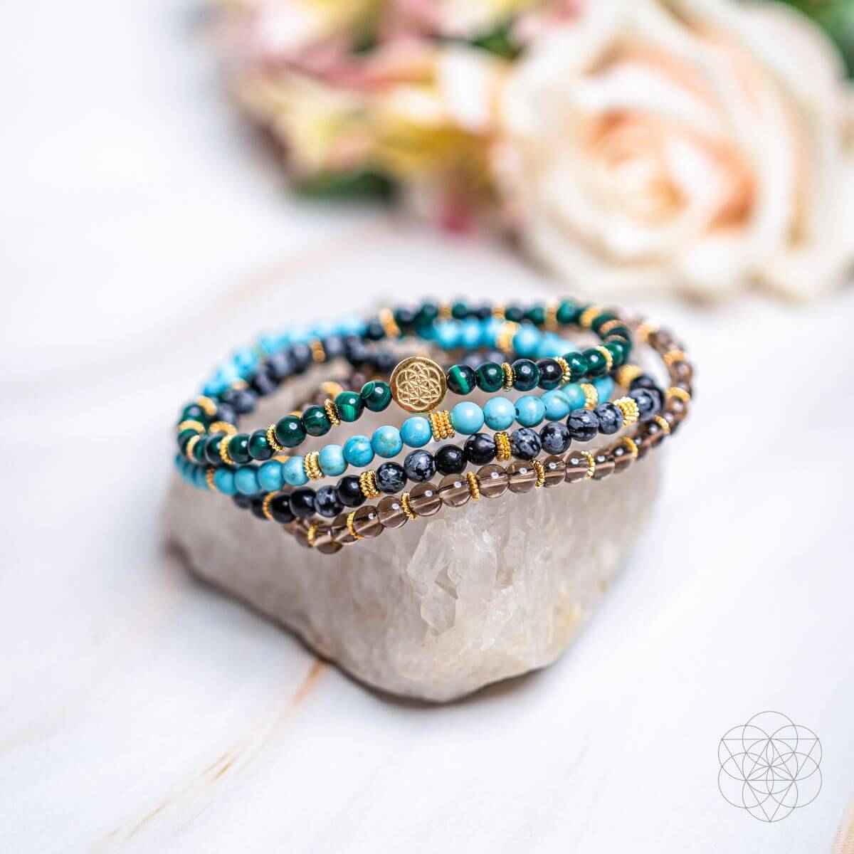 Four beaded bracelets laid on a light stone display, featuring turquoise, teal, and gold beads
