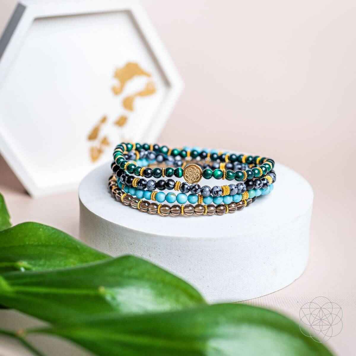 Stack of four beaded bracelets with turquoise, teal, and gold beads and a round center charm