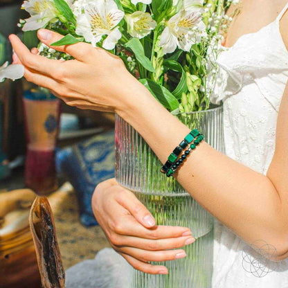 Triple-style beaded bracelet set in green and black worn on an arm near flowers