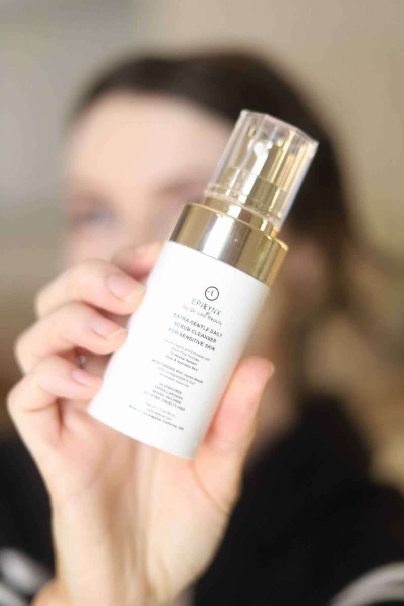 Hand holding EpiLynx gentle exfoliating face scrub bottle with gold pump