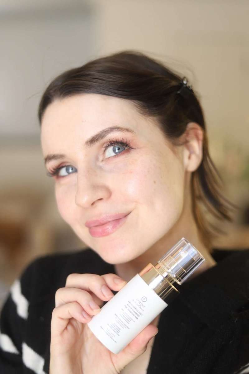 Gentle exfoliating face scrub bottle held near cheek; small white bottle with label