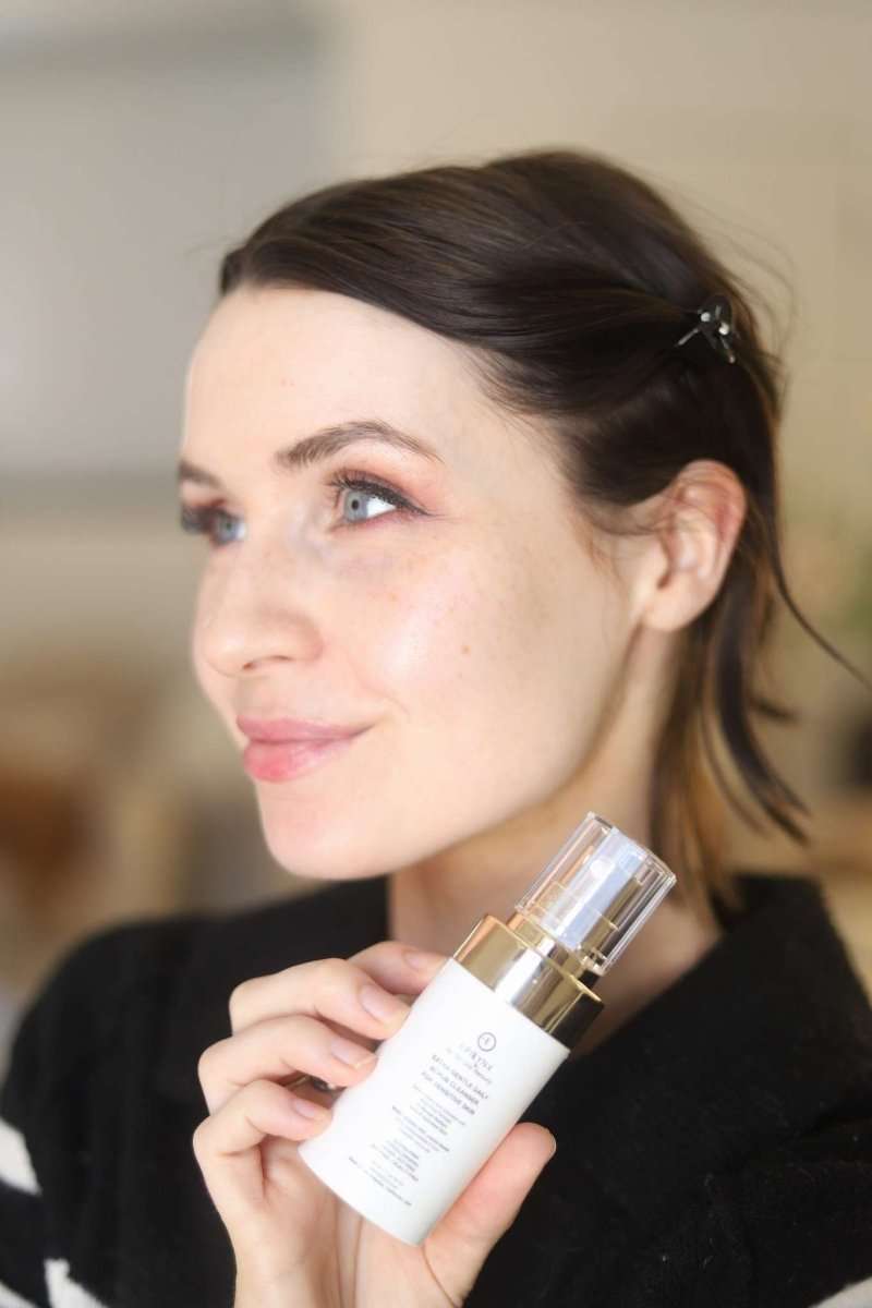 Woman holding EpiLynx scrub cleanser bottle near face with gold pump