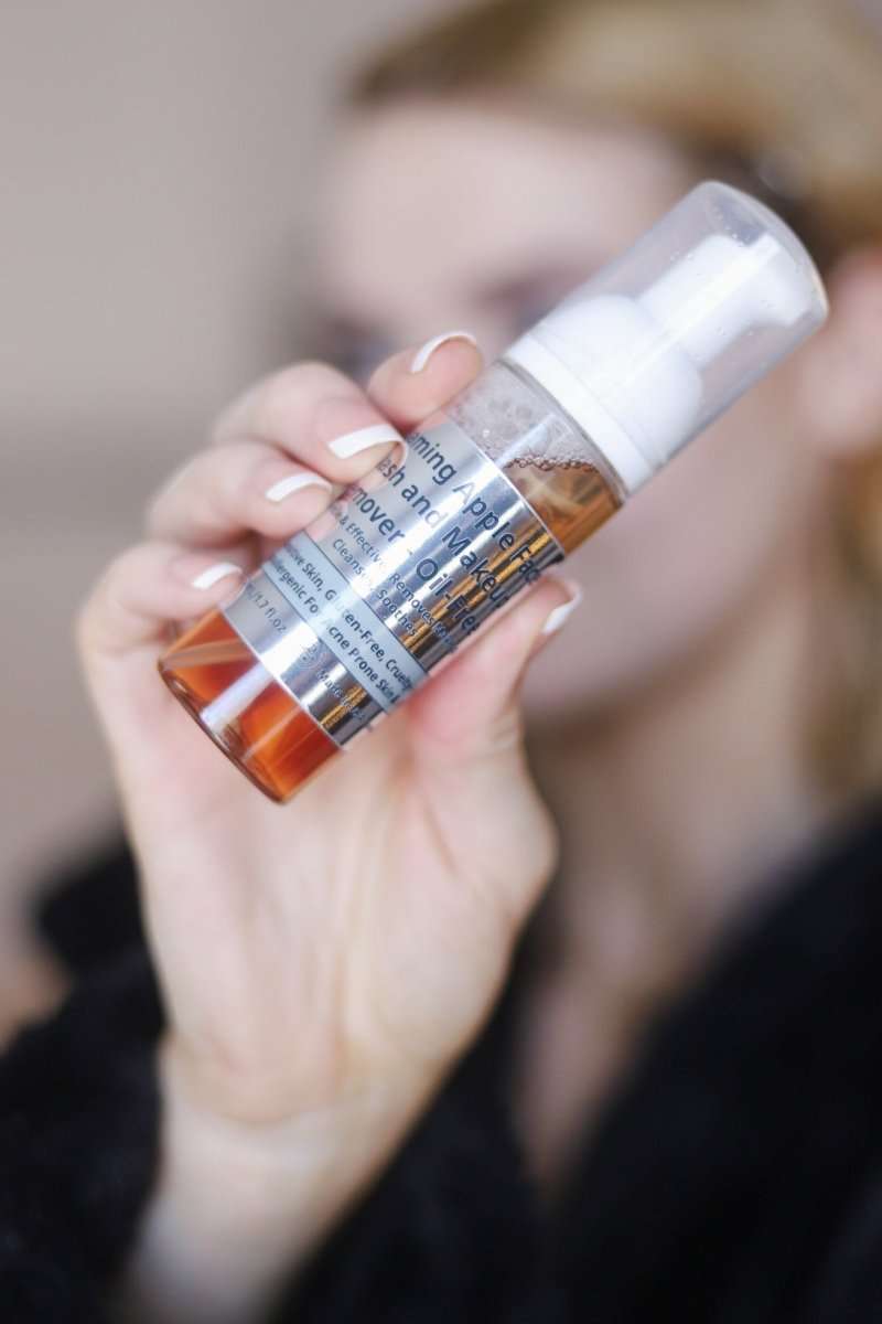 Gentle foaming facial cleanser bottle with white pump, amber liquid, held in hand