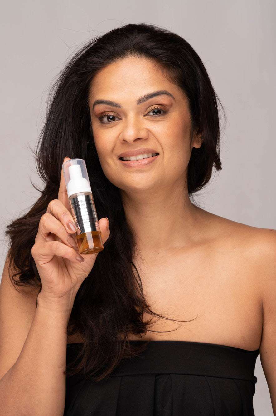 Woman holding foaming facial cleanser bottle near cheek
