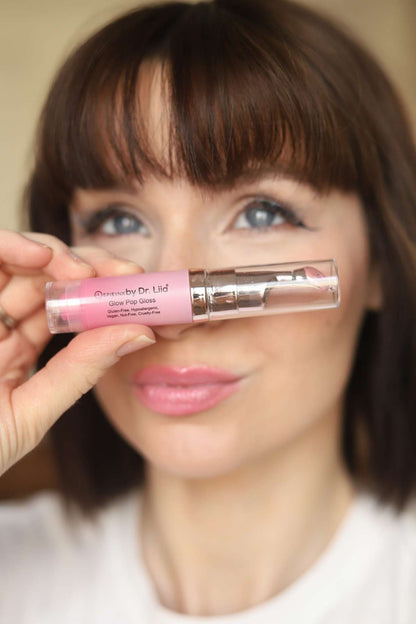 Pink lip gloss and lip treatment bottle held near lips with glossy pink sheen
