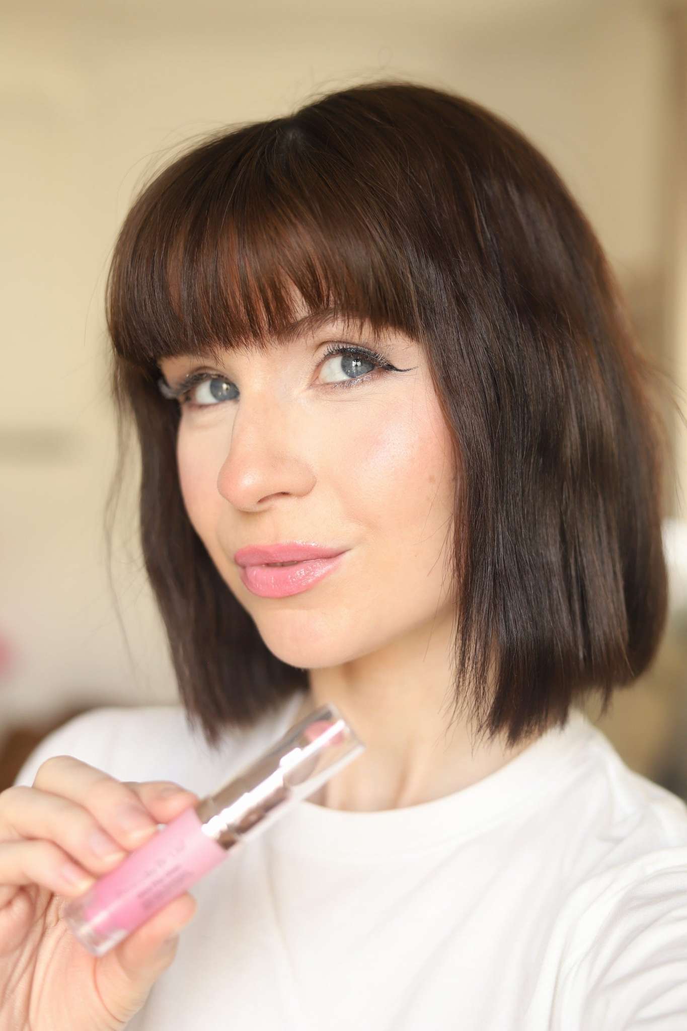 Woman applying pink lip gloss with clear applicator wand, glossy lips finish