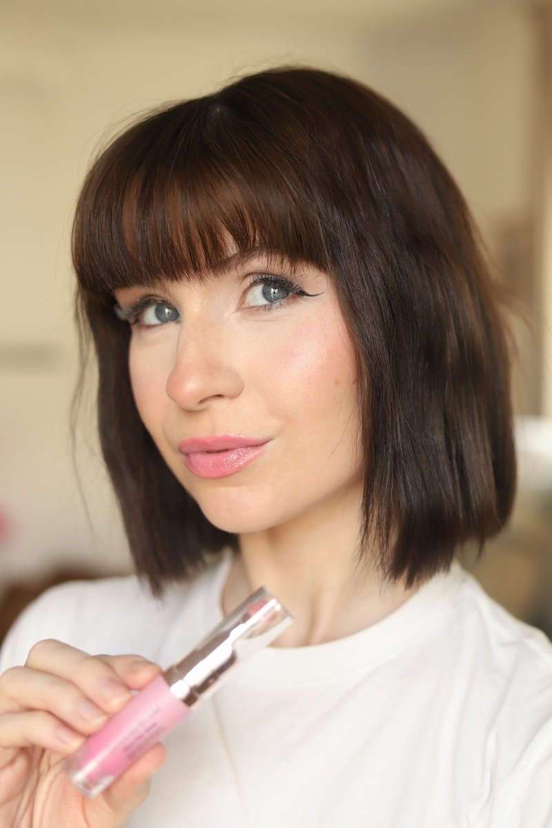 Woman holding clear applicator wand with pink lip gloss, glossy lips