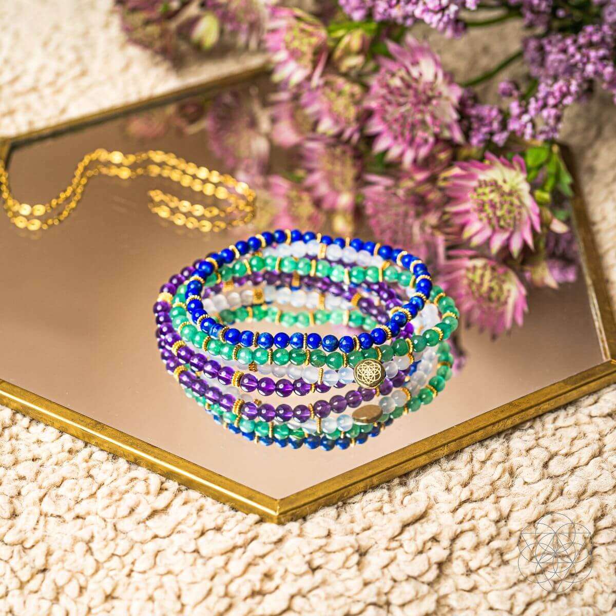 Four beaded bracelets on gift box with gold charm, blue, green, purple and white beads
