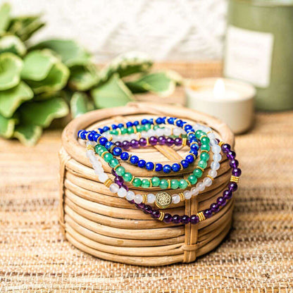 Four beaded bracelets in wooden bowl with gold charm, blue, green, purple and white beads