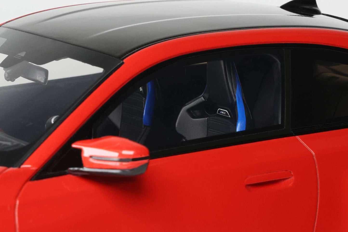 Red die-cast car side mirror and door close-up with black window trim and light detail