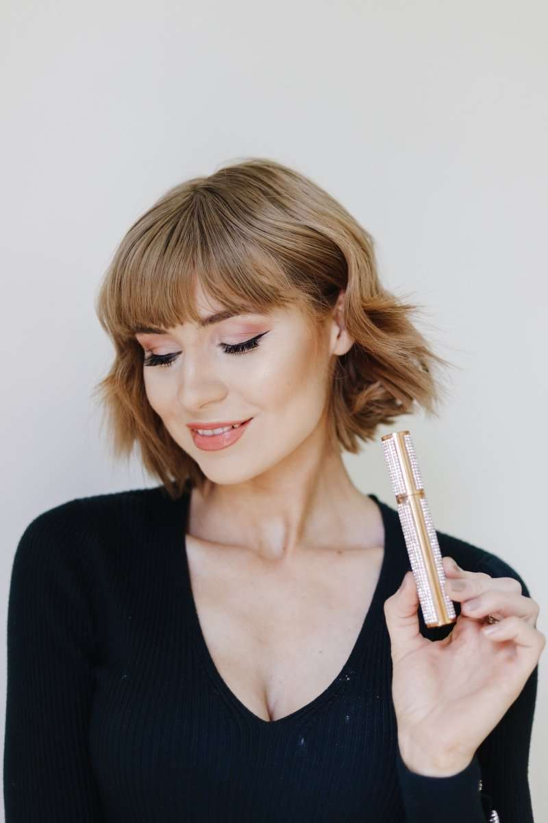 Diamond-look mascara container held by a woman with short blond hair and black wand.