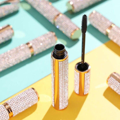 Diamond-look mascara tube with open black formula wand, bottles in a row.