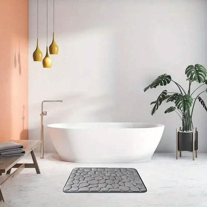 Grey cobblestone bath rug placed in front of a white bathtub