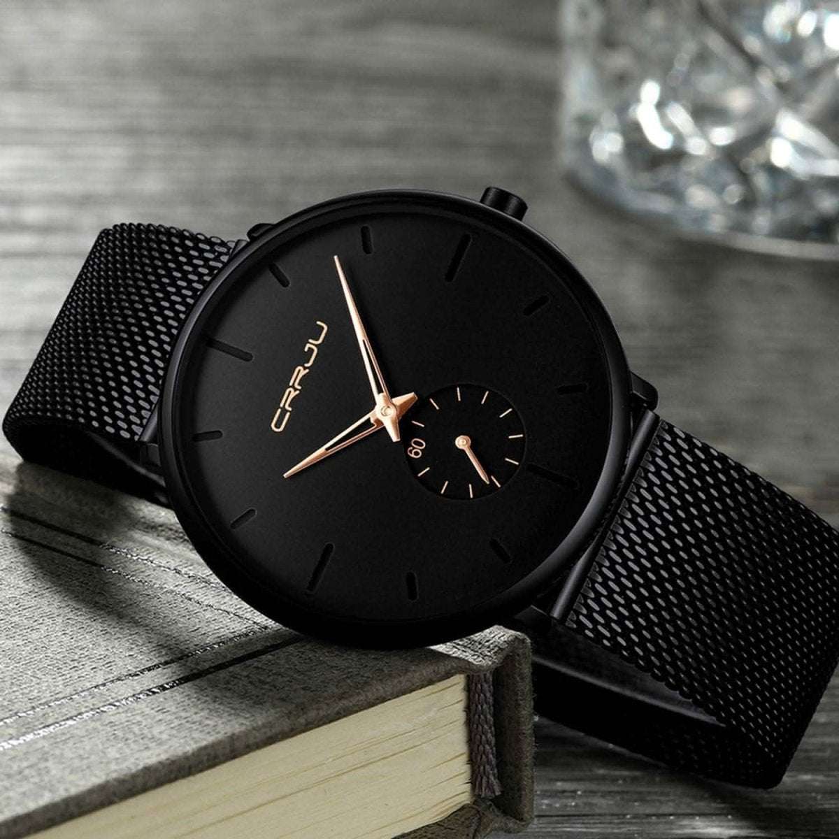 Minimalist black wrist watch with black mesh strap, black dial, gold hands and small subdial