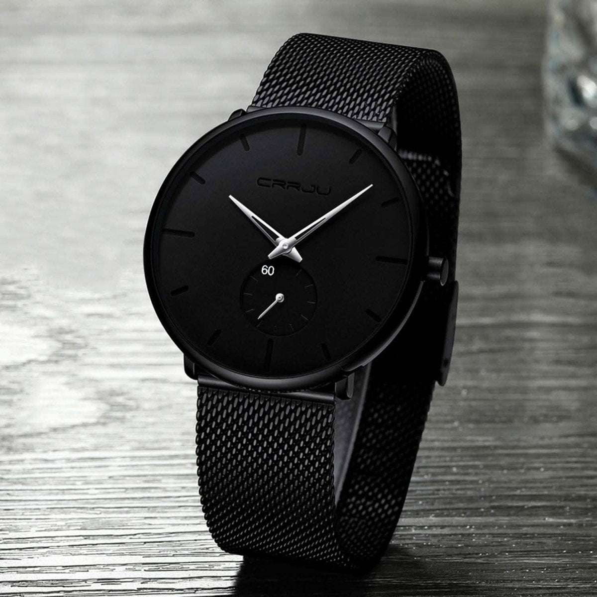 Black minimalist wrist watch with black dial and black mesh strap, angled view