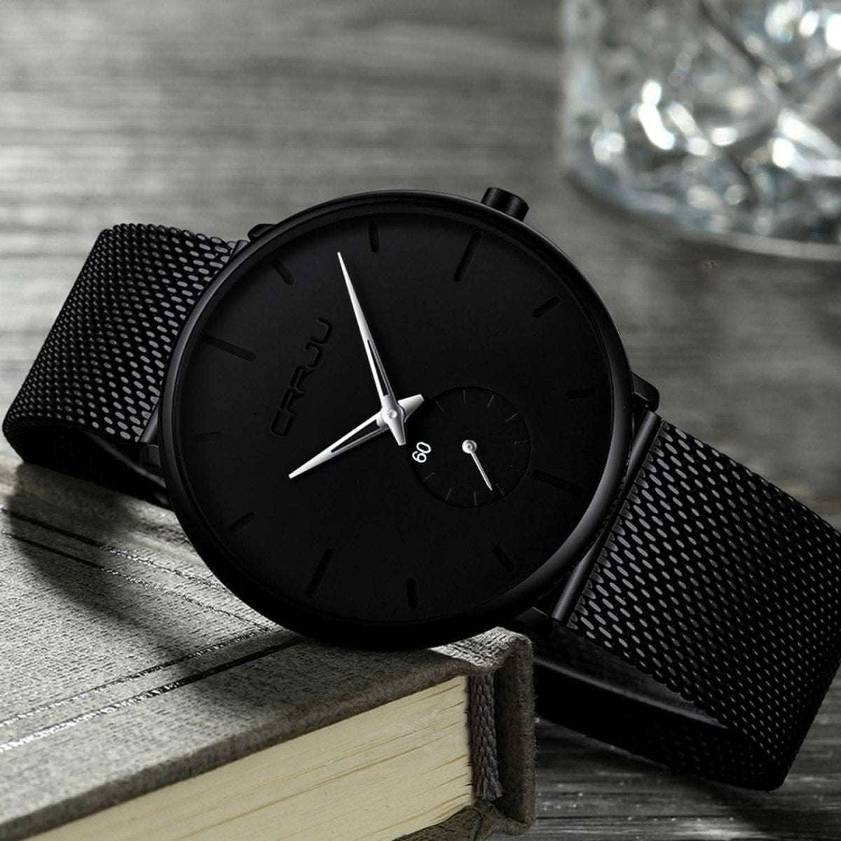 Black round wrist watch with black dial and black mesh strap, three-quarter view