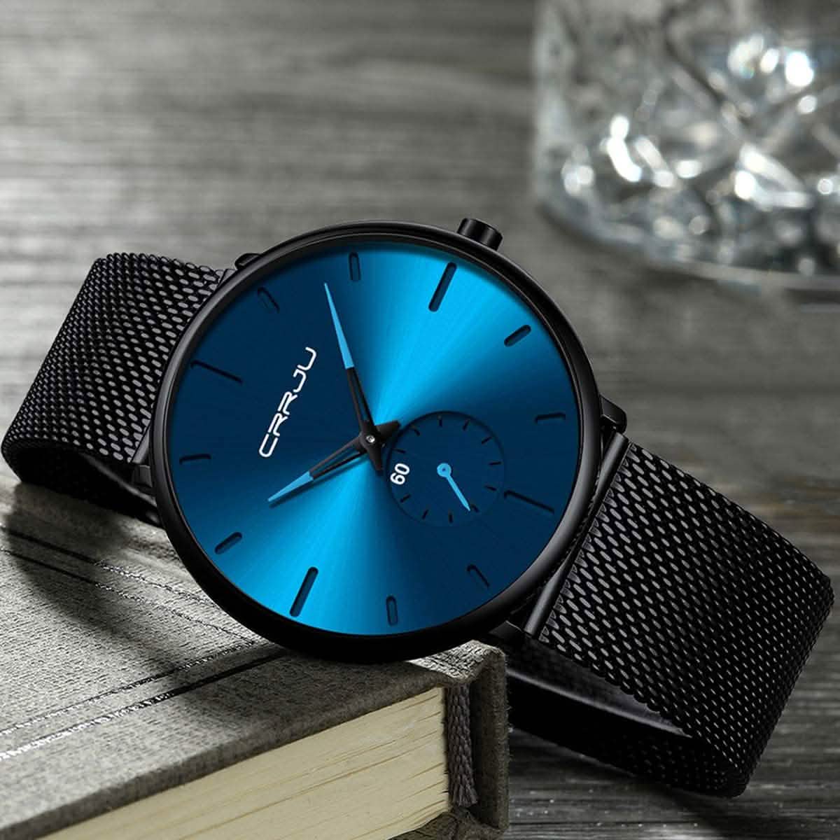 Blue minimalist wrist watch on stand, black mesh band and blue dial with teal highlights