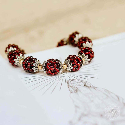 Natural garnet healing bracelet laid flat, red beads with gold flower accents