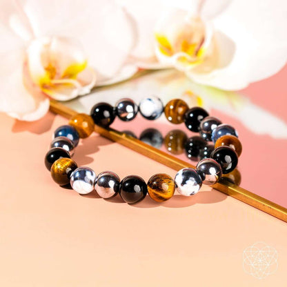Beaded bracelet with black, silver, and brown stones on a wooden baton