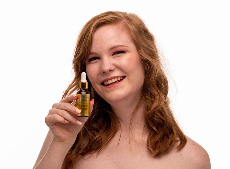 Facial serum bottle with black dropper held near face by smiling woman