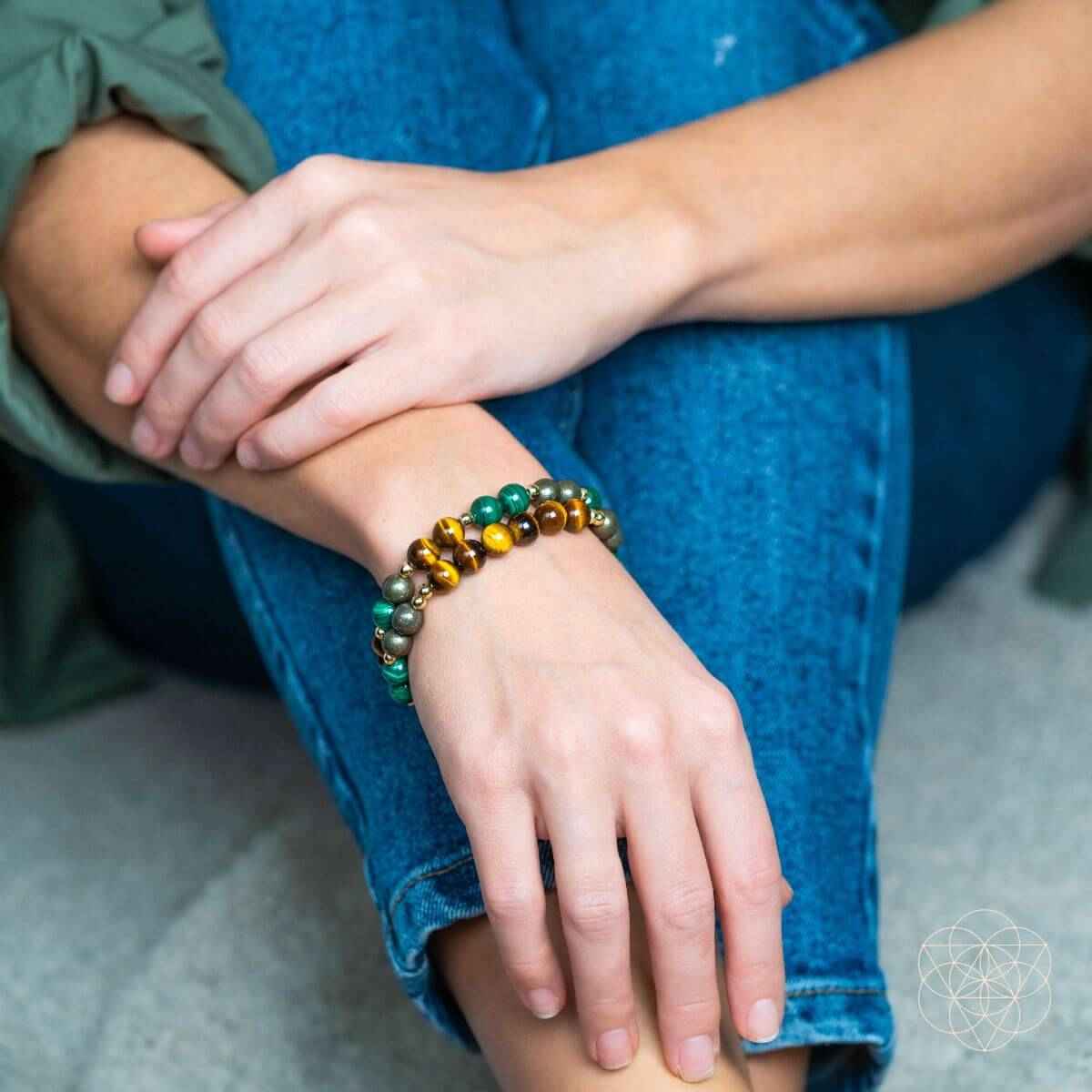 Beaded bracelets on wrist with tiger-eye brown, green, and silver beads and small gold charm