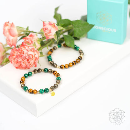 Two beaded bracelets laid on a white display with tiger-eye brown and green stone accents