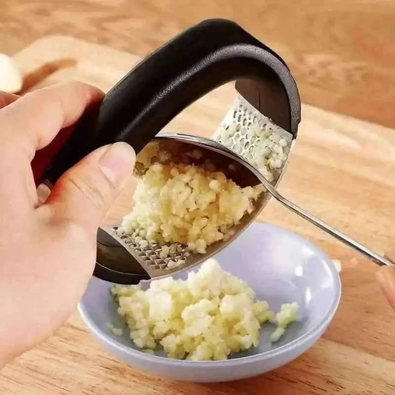 Garlic rocker press with black handle holding minced garlic in stainless perforations