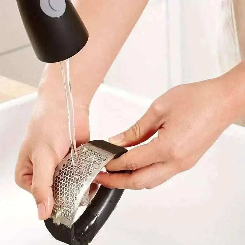 Garlic rocker press rinsed under running water, stainless perforated surface visible
