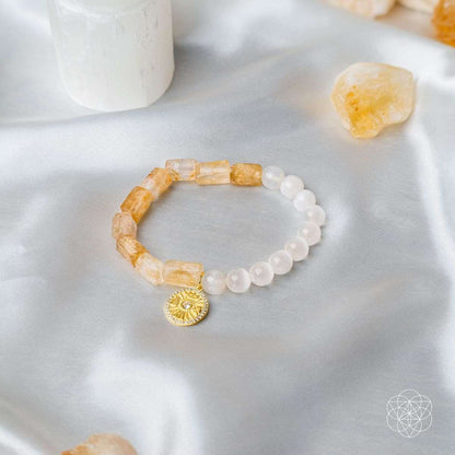 Citrine and selenite bracelet with gold sun medallion charm on light fabric