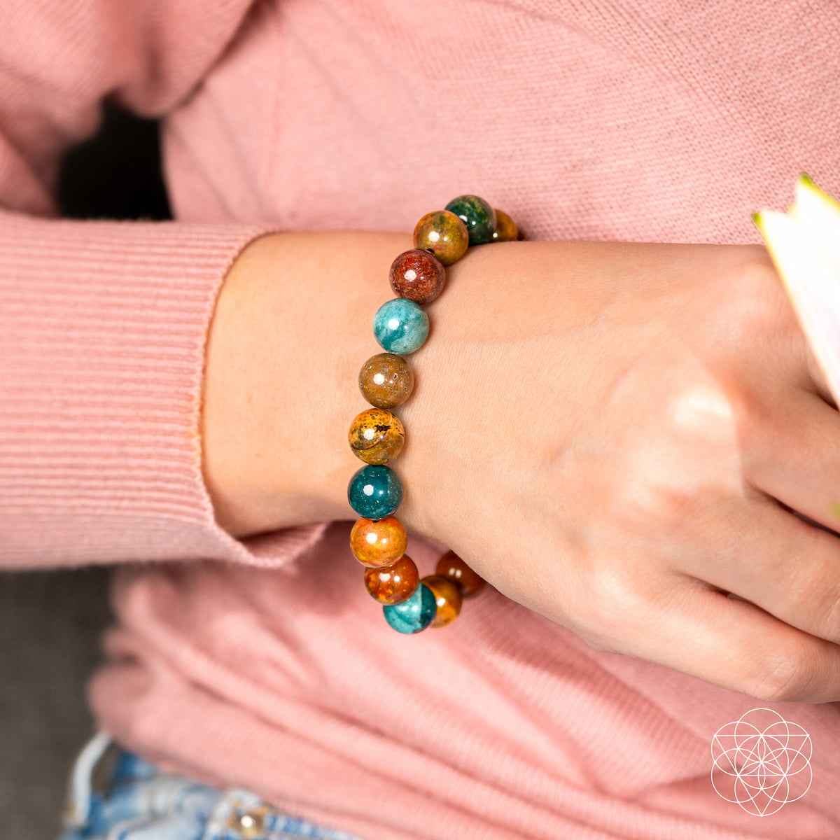 Beaded bracelet on wrist with teal, orange, and dark green round gemstone beads