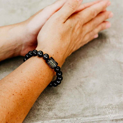 Obsidian protection bracelet on wrist, dark beads with a small gold-tone square charm