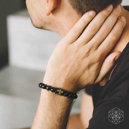 Obsidian bead protection bracelet on wrist with dark beads and central gold-tone charm