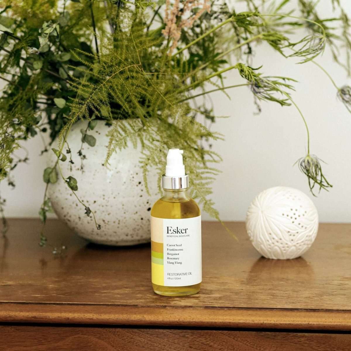 Restorative body oil bottle on a wooden surface beside flowers and white decor